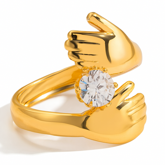Gold ring with a diamond set in a design resembling clasped hands on a white background