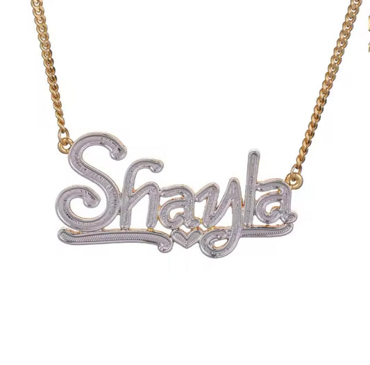 A gold-plated necklace with a custom double plated heart nameplate featuring the name 'Shayla' in a white, cursive script.