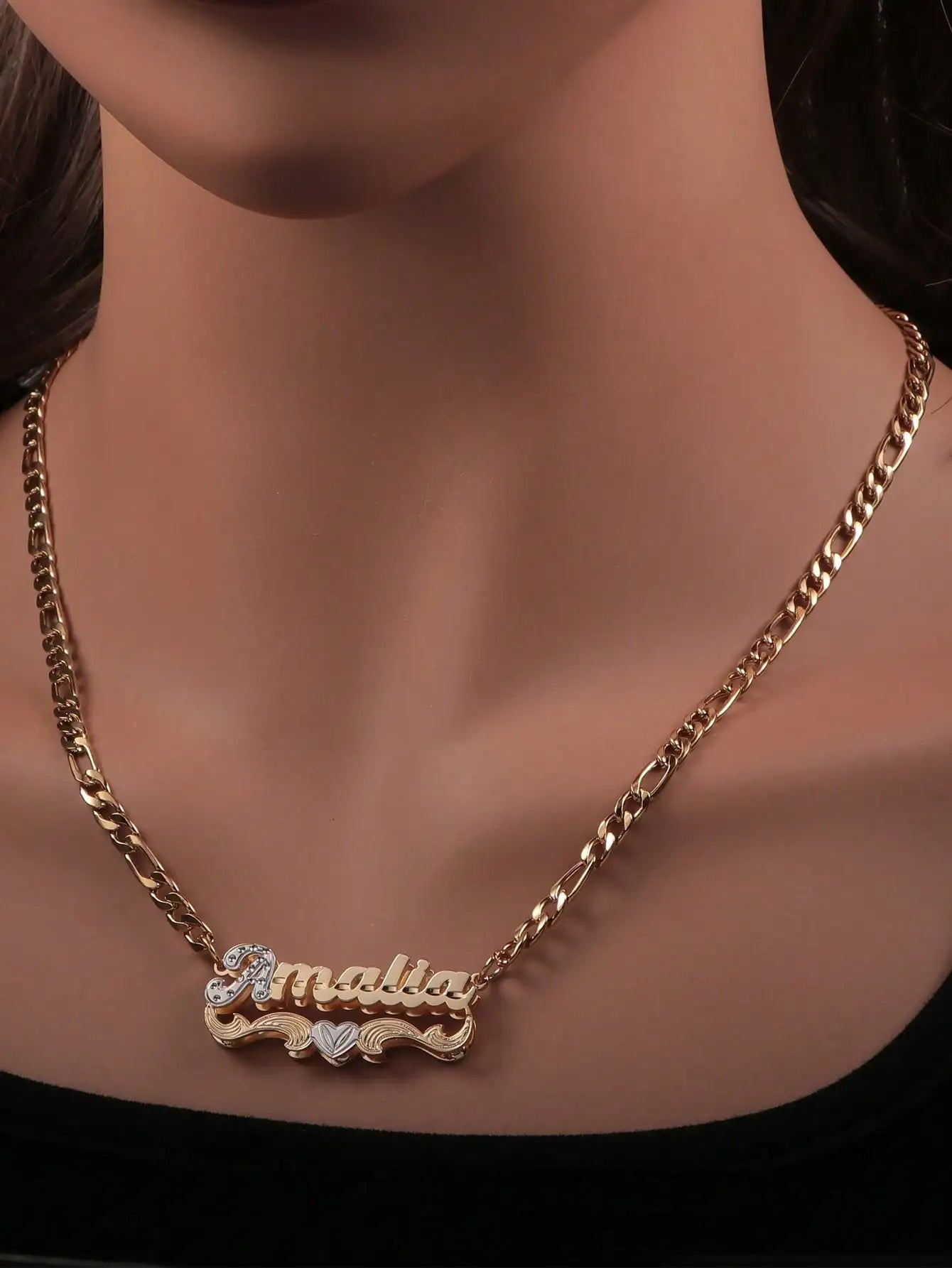 A gold chain necklace with a personalized nameplate pendant spelling 'malia' in gold script, accented with small clear rhinestones and a small heart, shown on a mannequin bust.