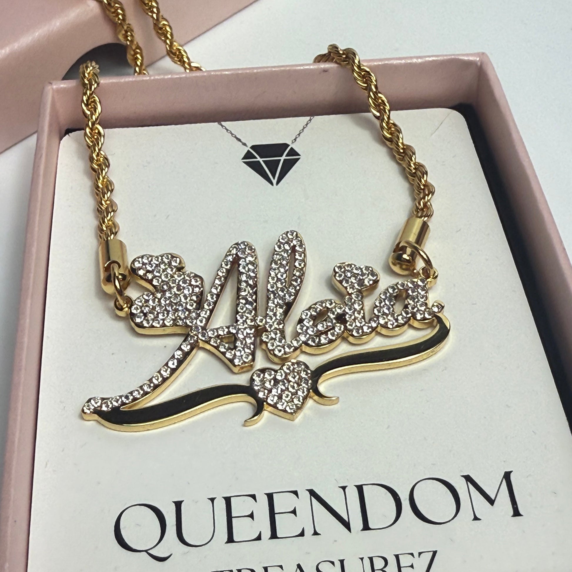 Gold necklace with decorative elements on a 'Queendom Treasurez' branded card.