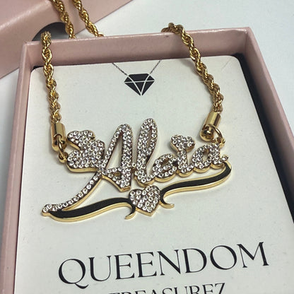 Gold necklace with decorative elements on a 'Queendom Treasurez' branded card.
