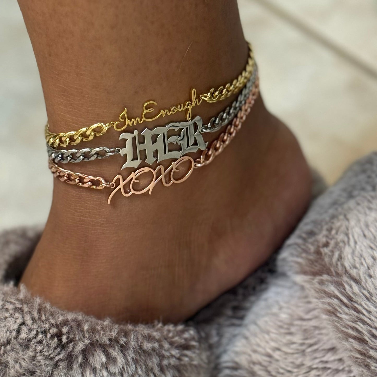 Ankle with multiple gold silver and rose gold bracelets on a neutral background