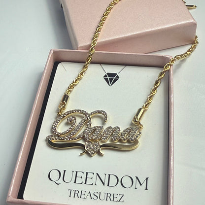 Gold necklace with decorative pendant on a QUEENDOM TREASUREZ branded card.