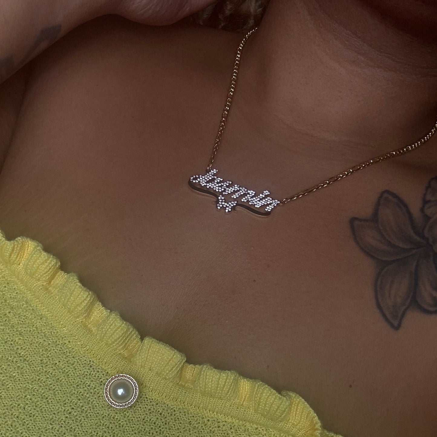 Necklace with 'Lover' pendant on a person's neck, with a green garment and tattoo visible.