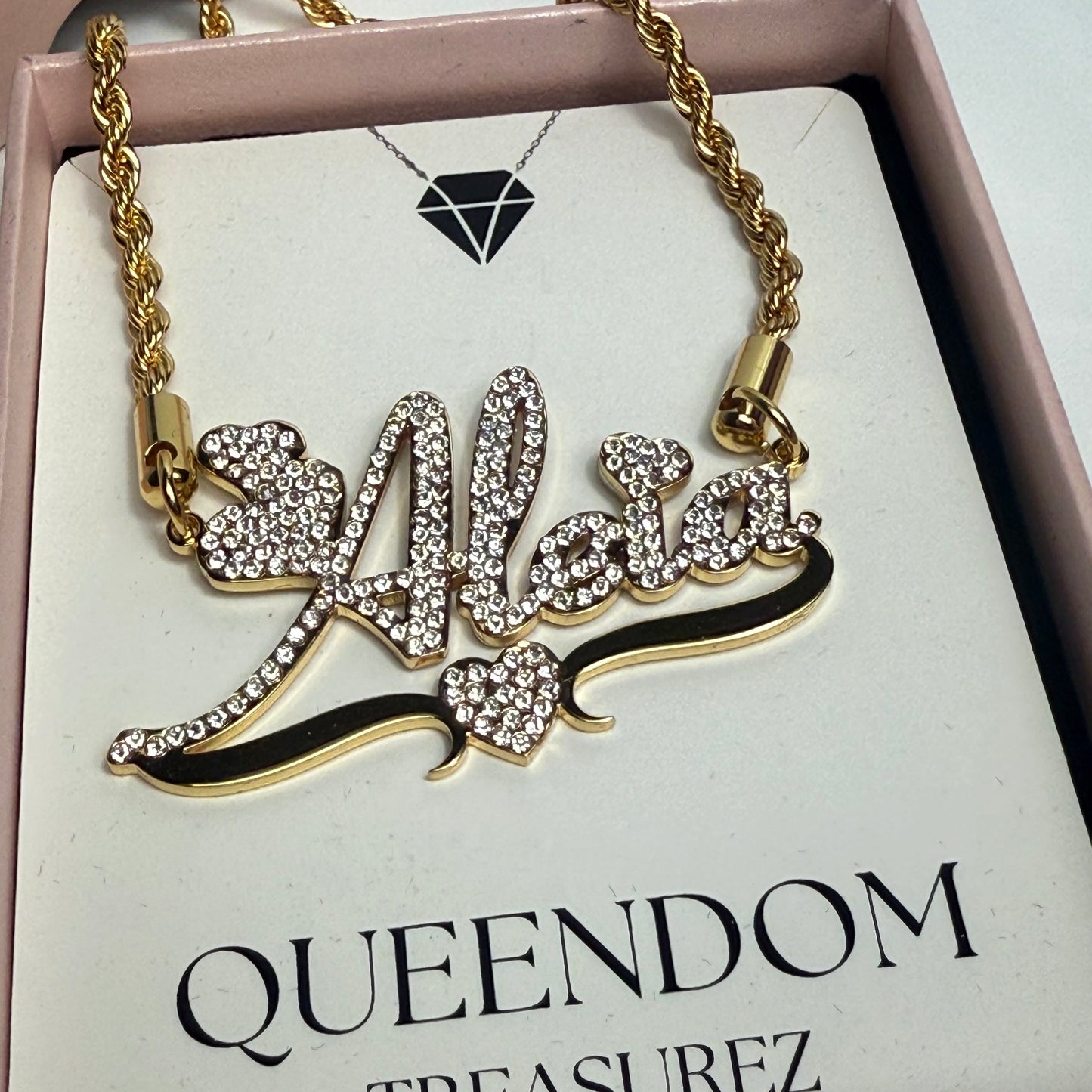 Gold necklace with a decorative pendant on a 'Queendom Treasurez' branded card.