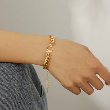 Gold chain bracelet on a wrist with a neutral background