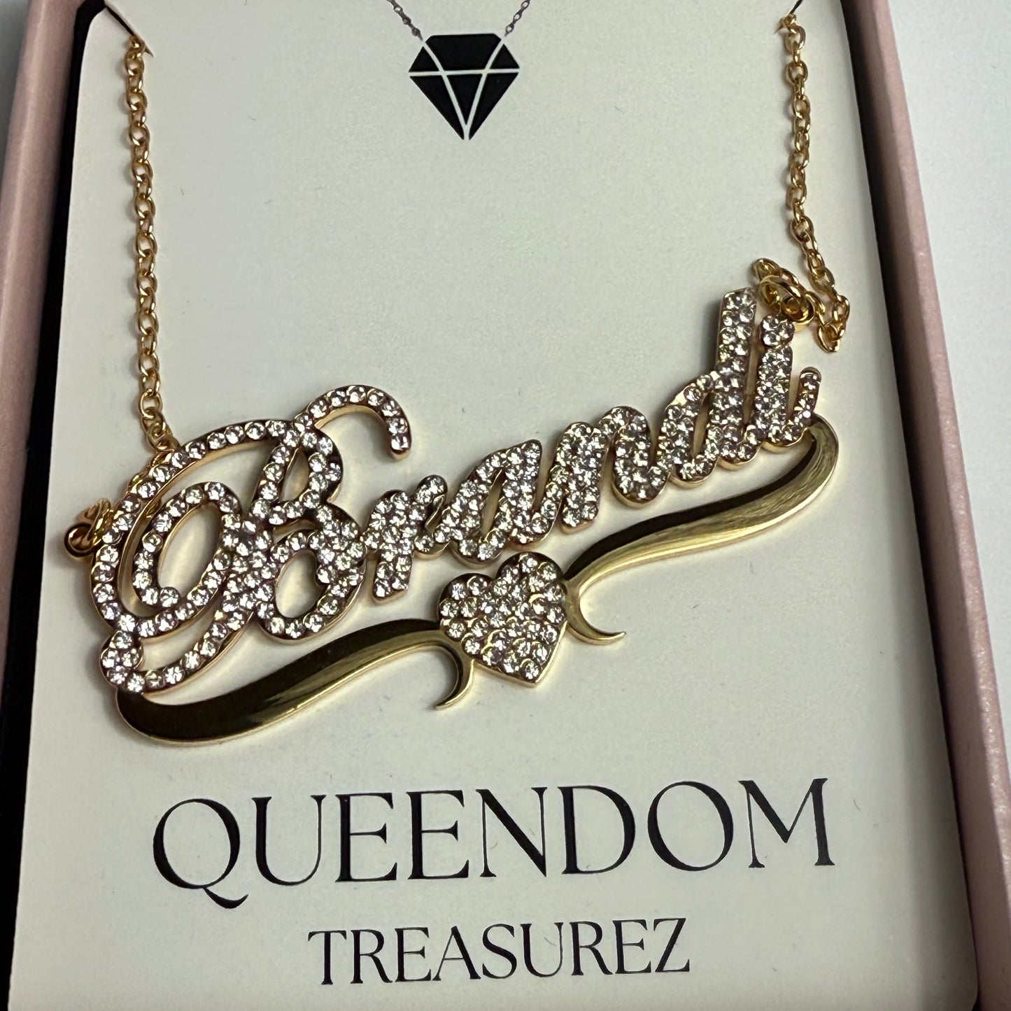 Gold necklace with intricate design on a 'QUEENDOM TREASUREZ' branded card.
