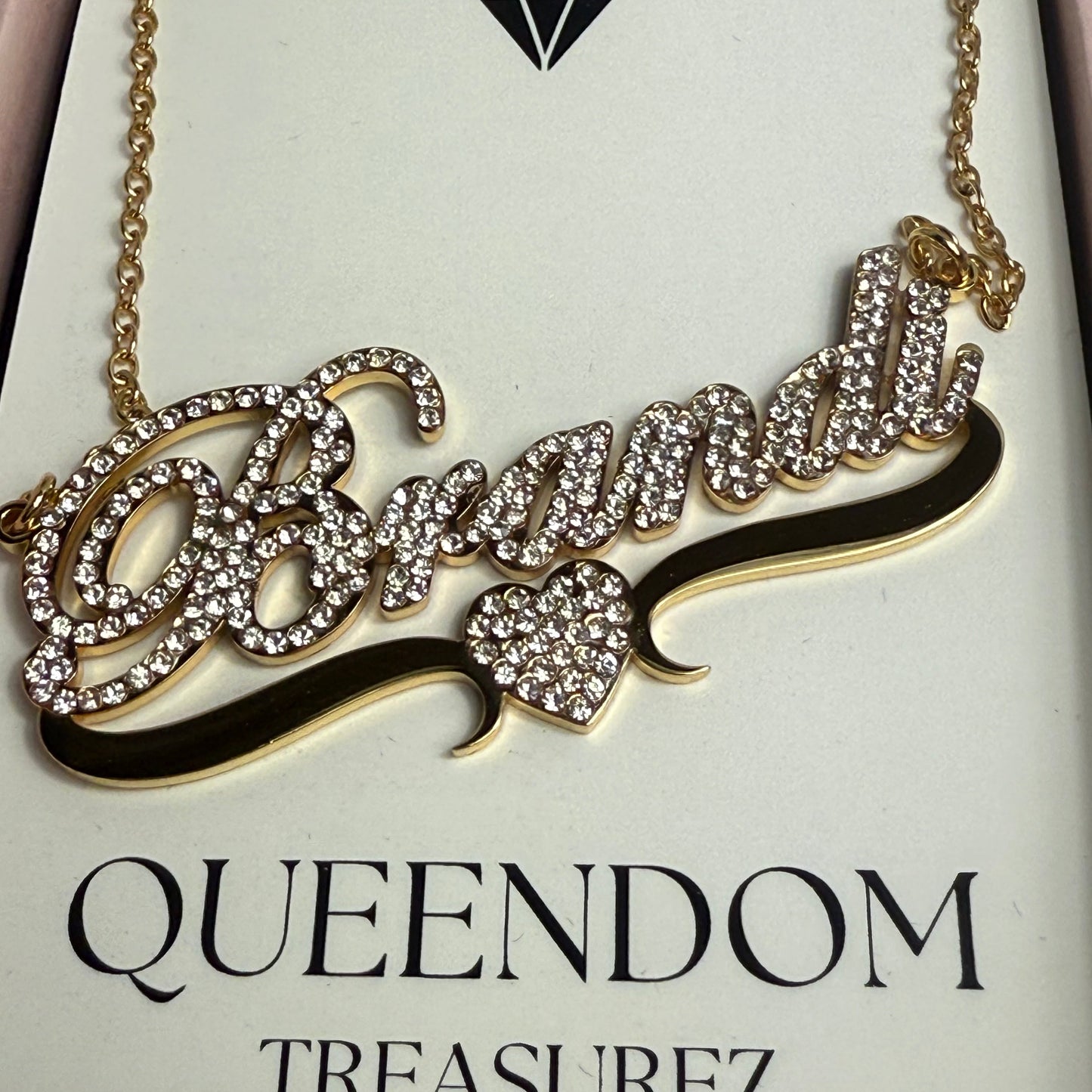 Decorative necklace with intricate design on a 'QUEENDOM TREASUREZ' branded card.
