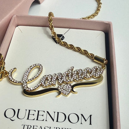 Gold bracelet with intricate design on a 'QUEENDOM TREASUREZ' branded box.