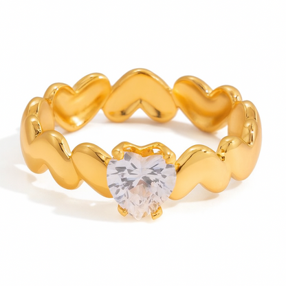 Gold ring with heart-shaped design and clear gemstone on a white background