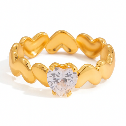Gold ring with heart-shaped design and clear gemstone on a white background