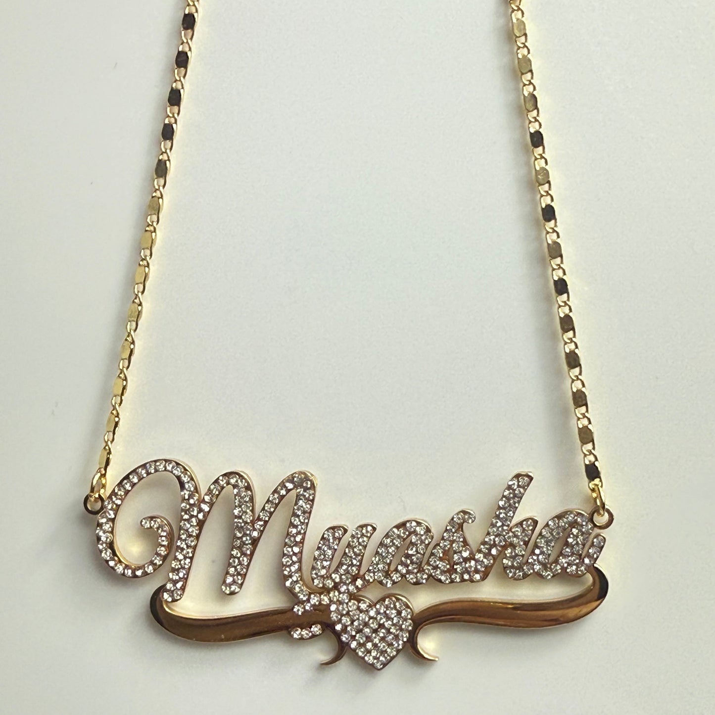 Gold necklace with a leaf-shaped pendant on a light gray background