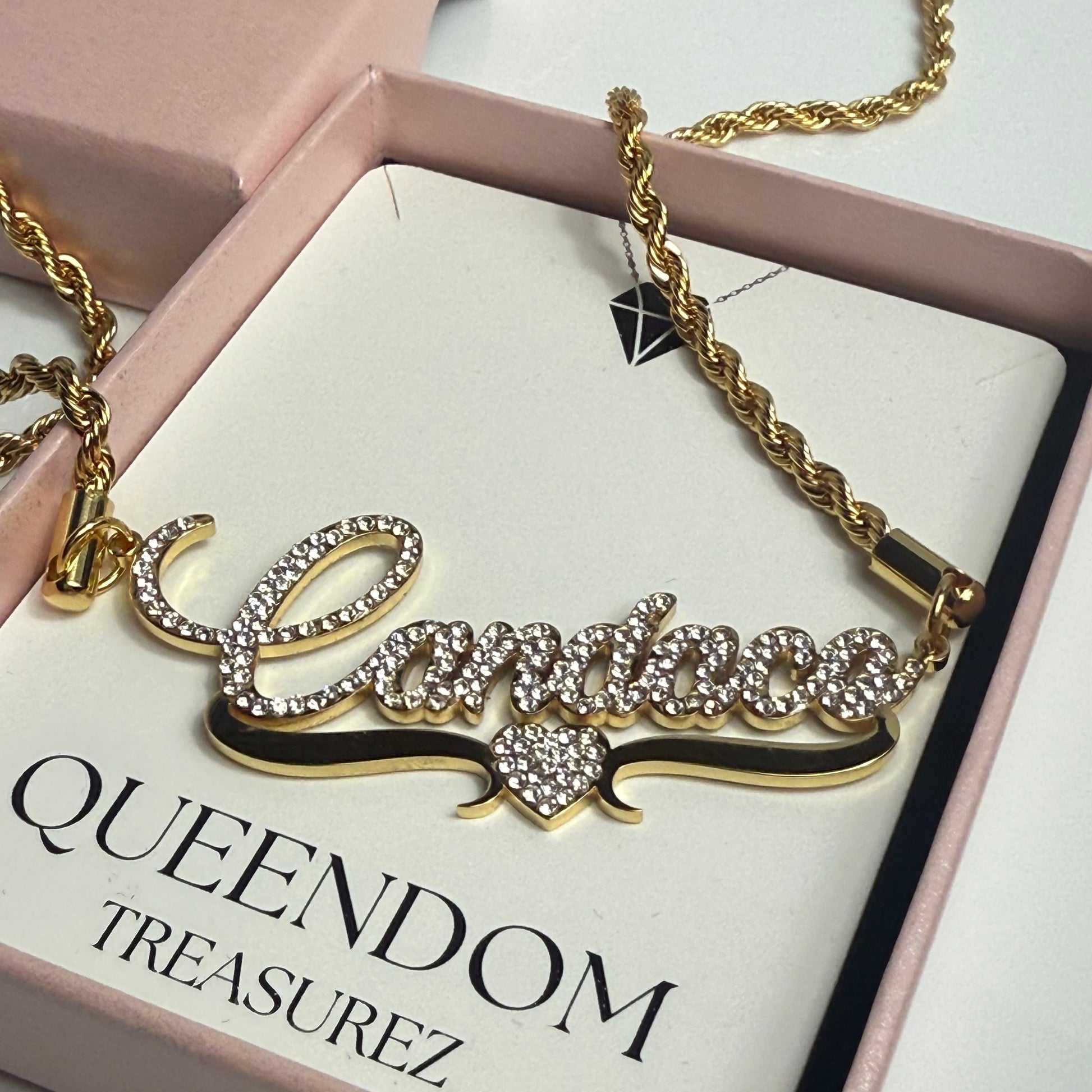 Gold necklace with decorative elements on a 'QUEENDOM TREASUREZ' branded card.