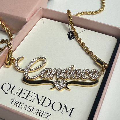 Gold necklace with decorative elements on a 'QUEENDOM TREASUREZ' branded card.