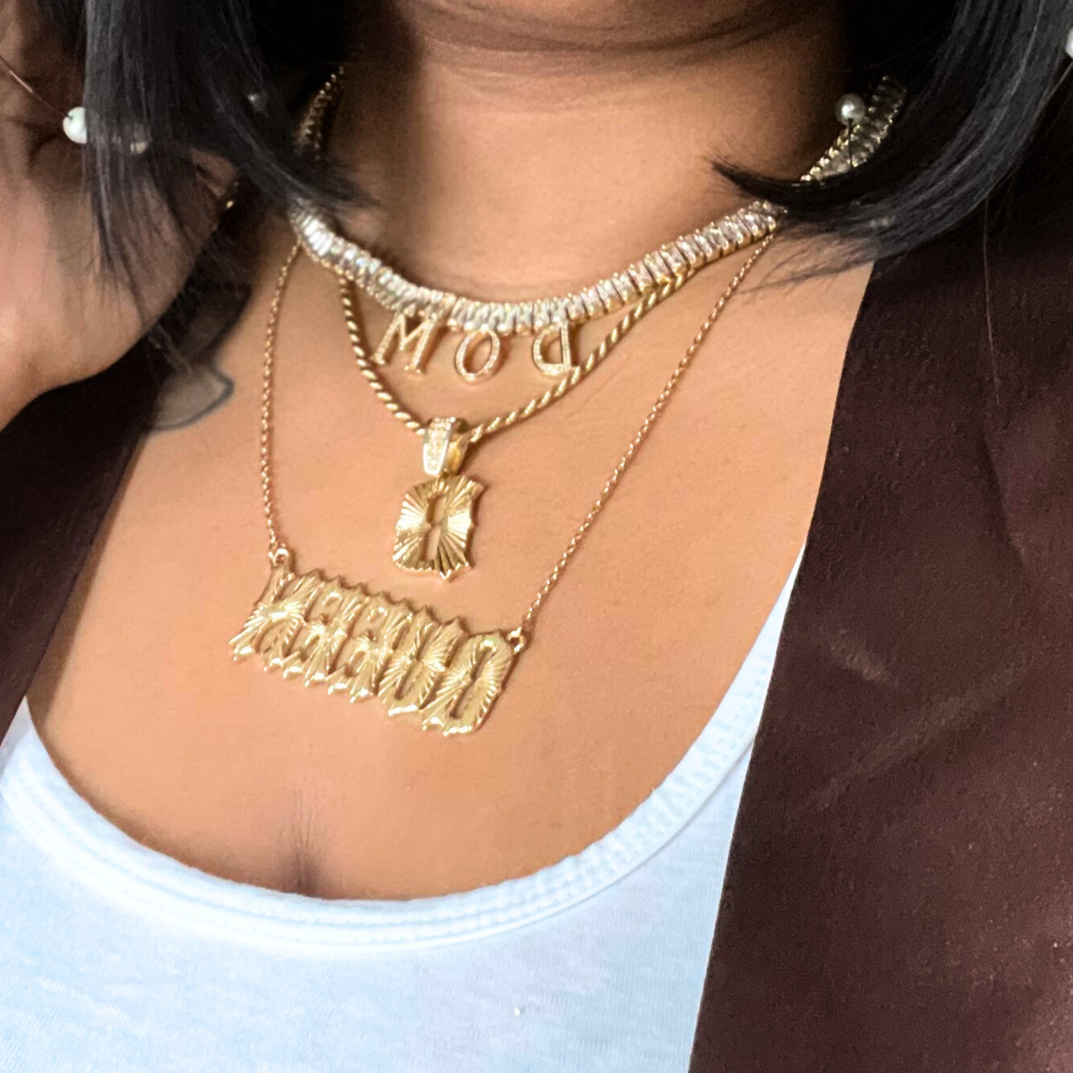 Close-up of a person wearing gold necklaces with visible branding.