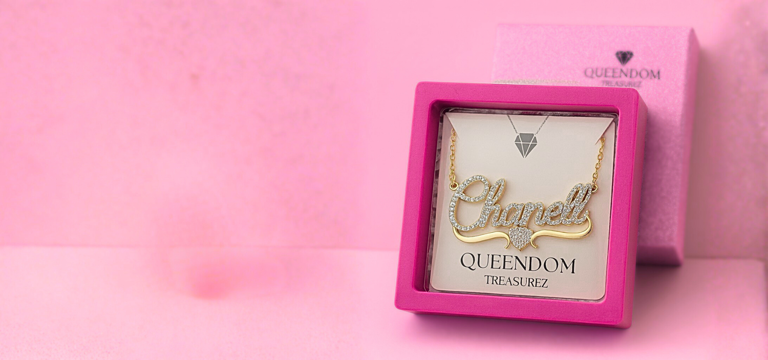Gold necklace with 'Elle' pendant in a pink 'QUEENDOM' box on a pink background