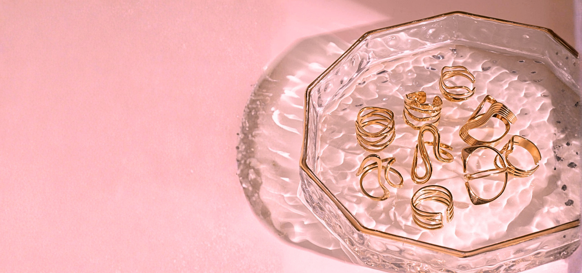 Gold spiral hair ties on a decorative glass dish with a pink background